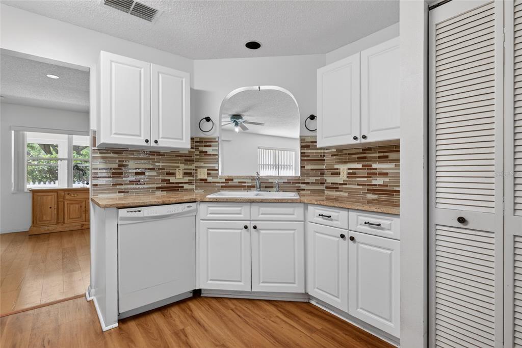 A kitchen features white cabinets, a mosaic tile backsplash, laminate countertops, and a white dishwasher — 9060 SW 96TH LANE UNIT B, OCALA, FL
