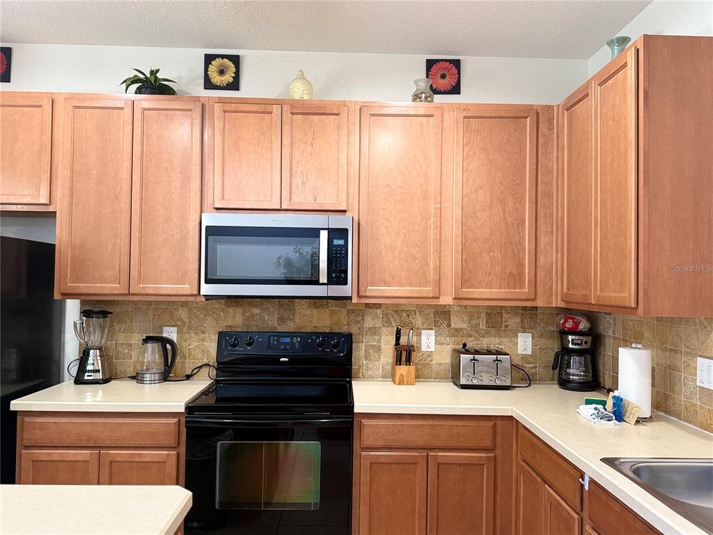 A kitchen features light wood cabinets, a black stove, a microwave, and a tiled backsplash — 2514 DHARMA CIRCLE, KISSIMMEE, FL
