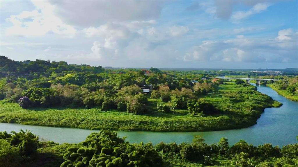An aerial view shows a winding river flowing through a lush, green landscape with a bridge — BARRIO CACAO, CAROLINA, PR