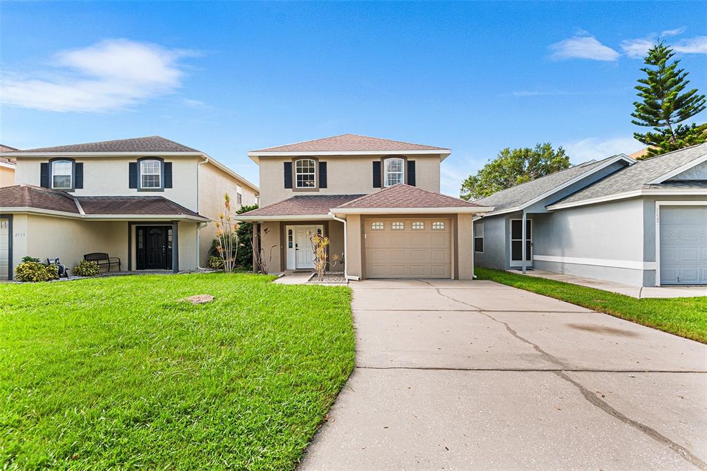 A two-story suburban house with a tan stucco exterior, a garage, and a front lawn — 2101 HATTERAS POINT, LAKELAND, FL