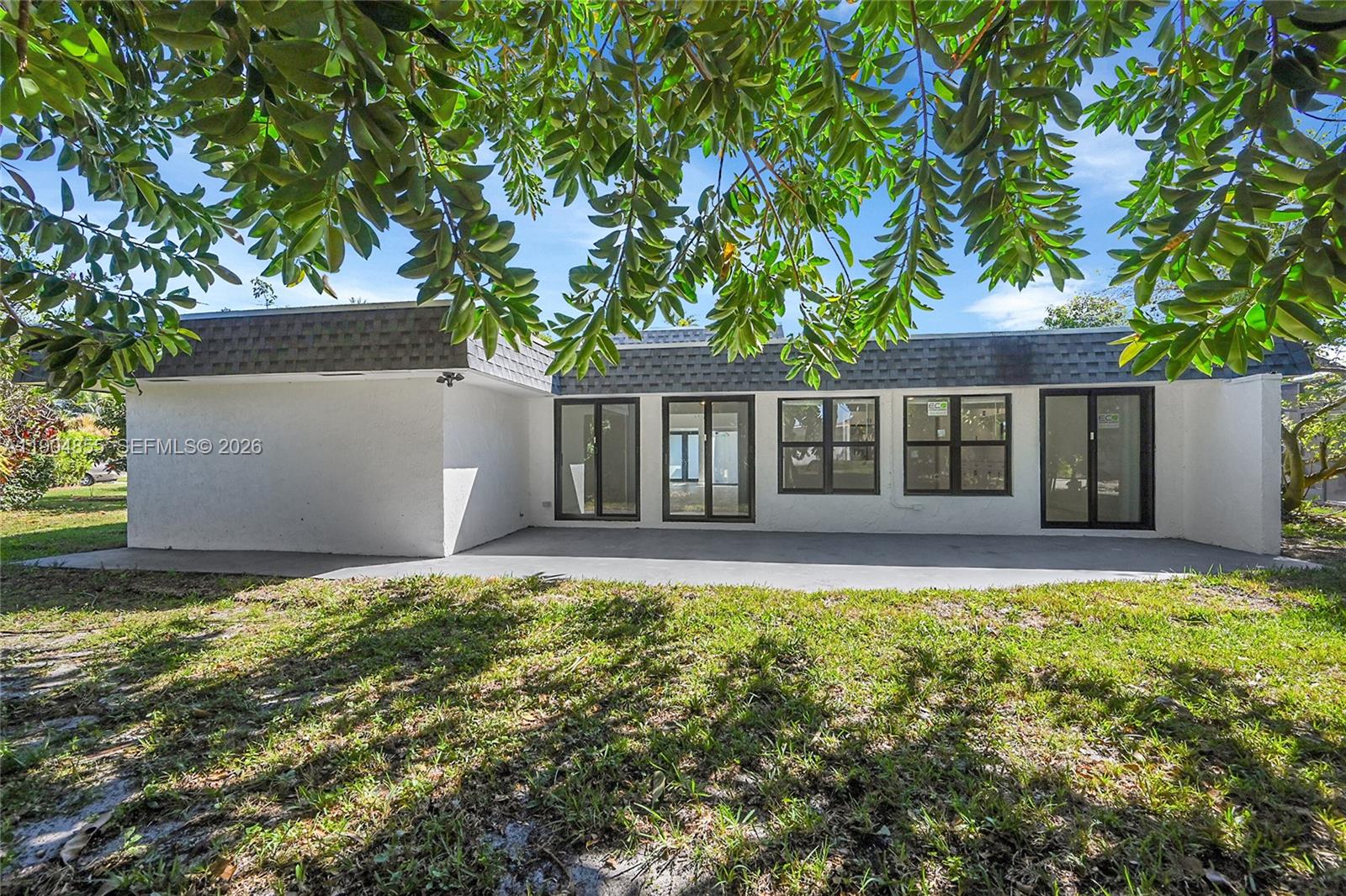 The exterior of a white house features a concrete patio and multiple glass doors — 4603 King Palm Dr, Tamarac FL 33319, TAMARAC, FL