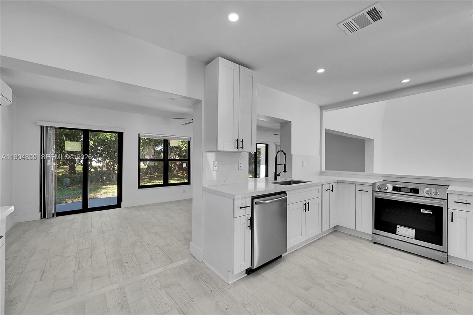 A modern kitchen features white cabinets, stainless steel appliances, and light wood-look tile flooring — 4603 King Palm Dr, Tamarac FL 33319, TAMARAC, FL