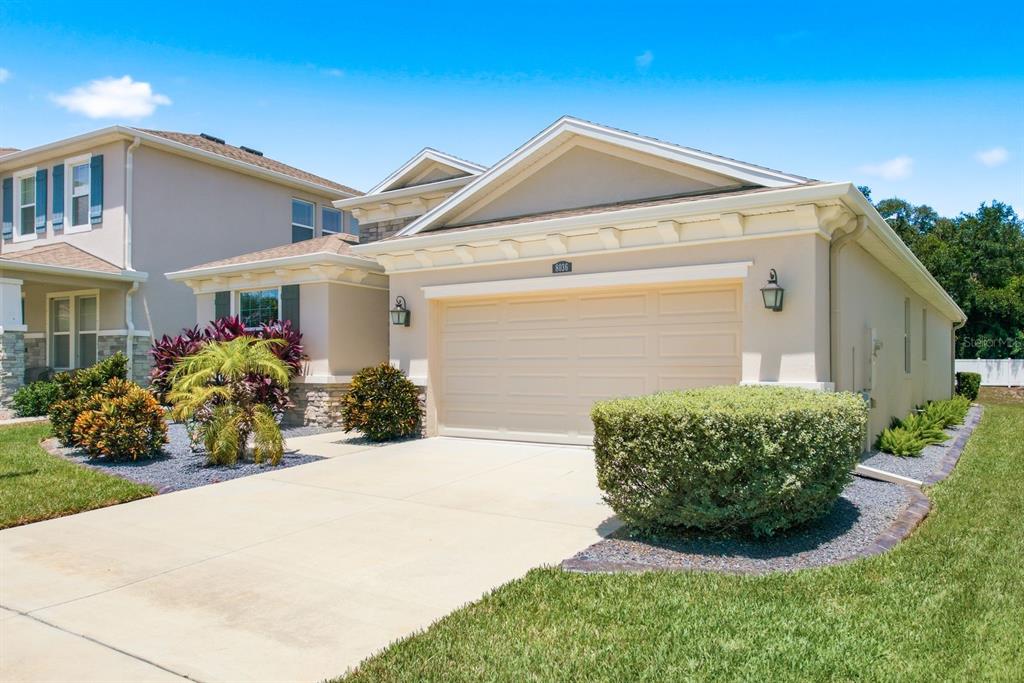 A beige single-story house with a two-car garage and landscaped front yard — 8036 PRAISE DRIVE, TAMPA, FL