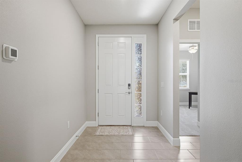 A bright entryway features light-colored tile flooring, neutral walls, and a white front door — 8036 PRAISE DRIVE, TAMPA, FL