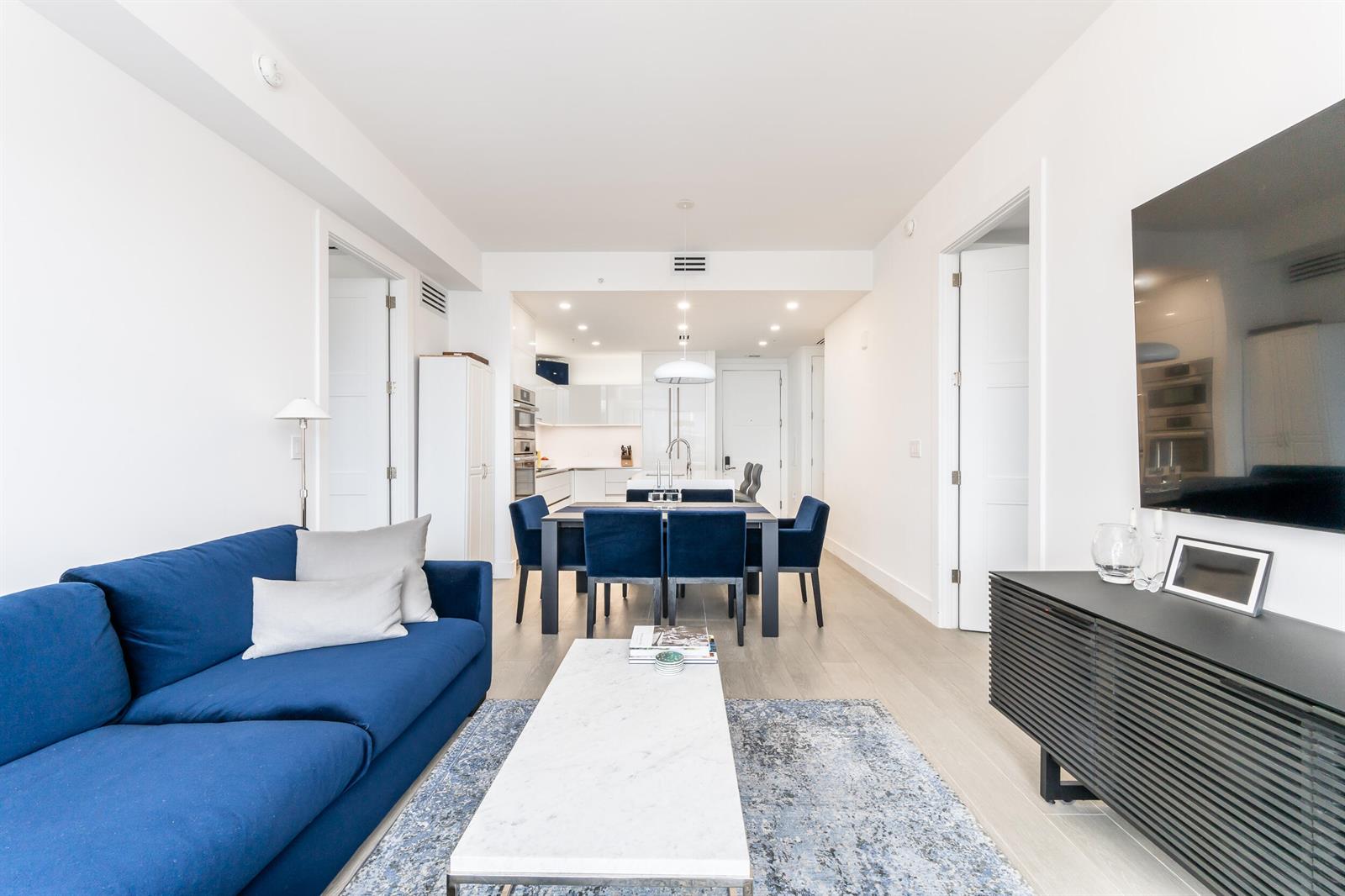 A modern living room and dining area feature a blue sofa, marble table, and kitchen — 155 E Boca Raton Road # 818, Boca Raton FL 33432, BOCA RATON, FL