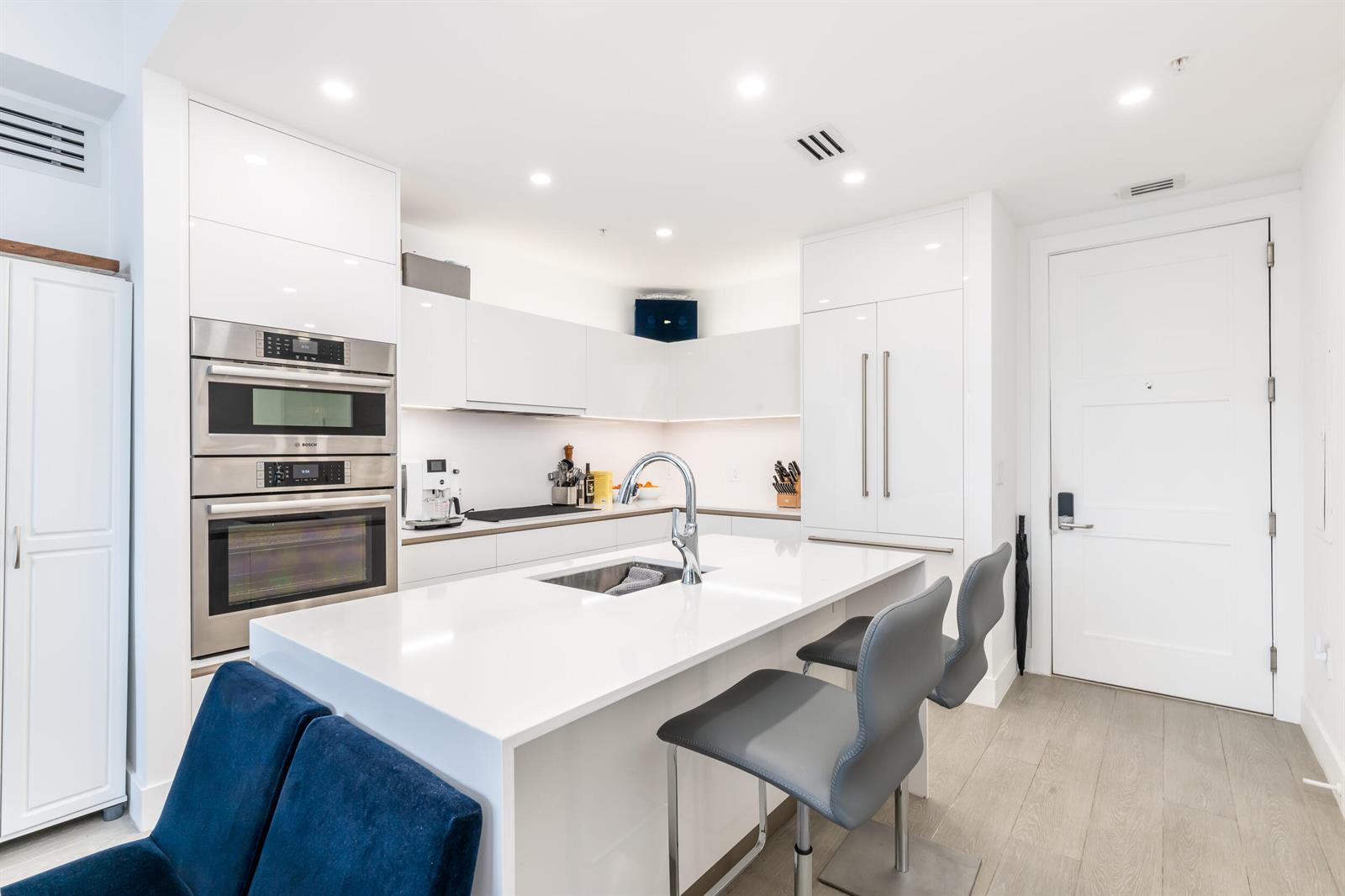 A modern kitchen features white cabinetry, stainless steel appliances, a quartz island, and gray barstools — 155 E Boca Raton Road # 818, Boca Raton FL 33432, BOCA RATON, FL