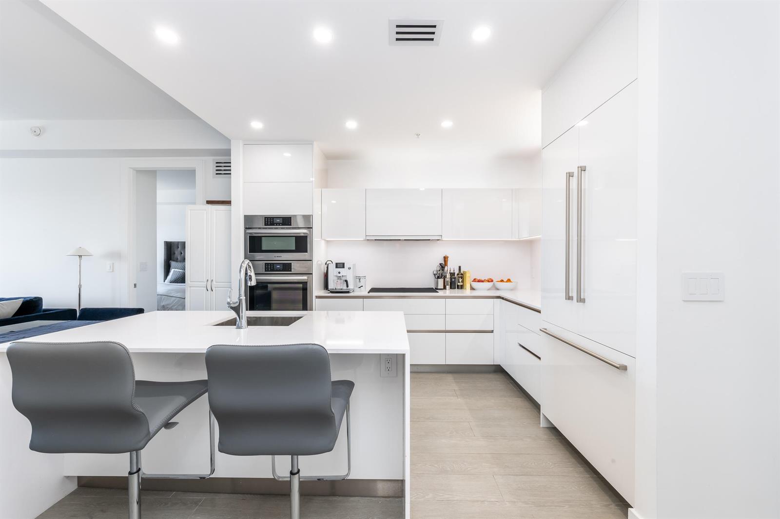A modern white kitchen features a central island with gray bar stools and stainless appliances — 155 E Boca Raton Road # 818, Boca Raton FL 33432, BOCA RATON, FL