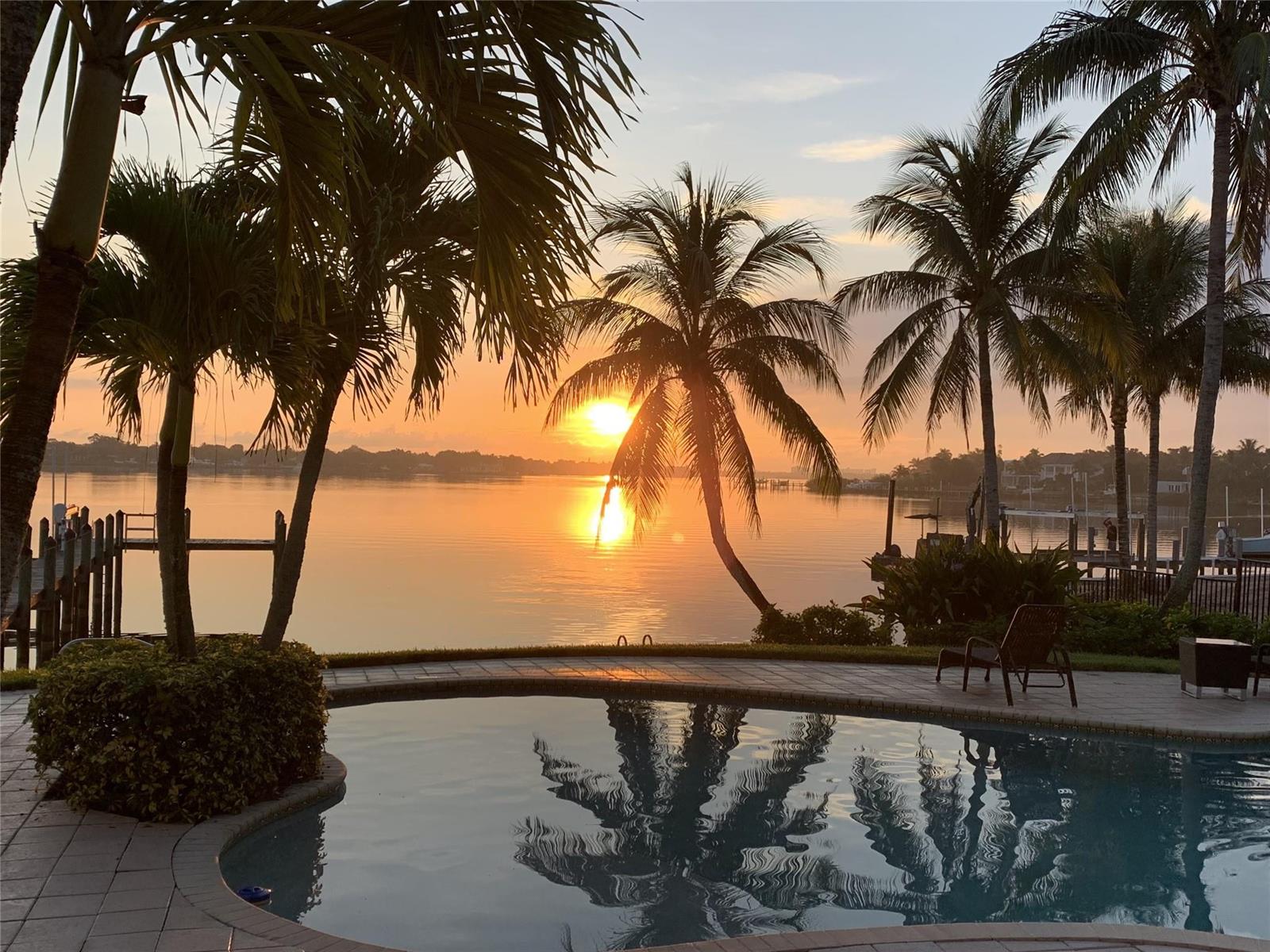 A swimming pool overlooks a calm bay at sunset with palm trees and boat docks — 19022 Loxahatchee River Road, Jupiter FL 33458, JUPITER, FL