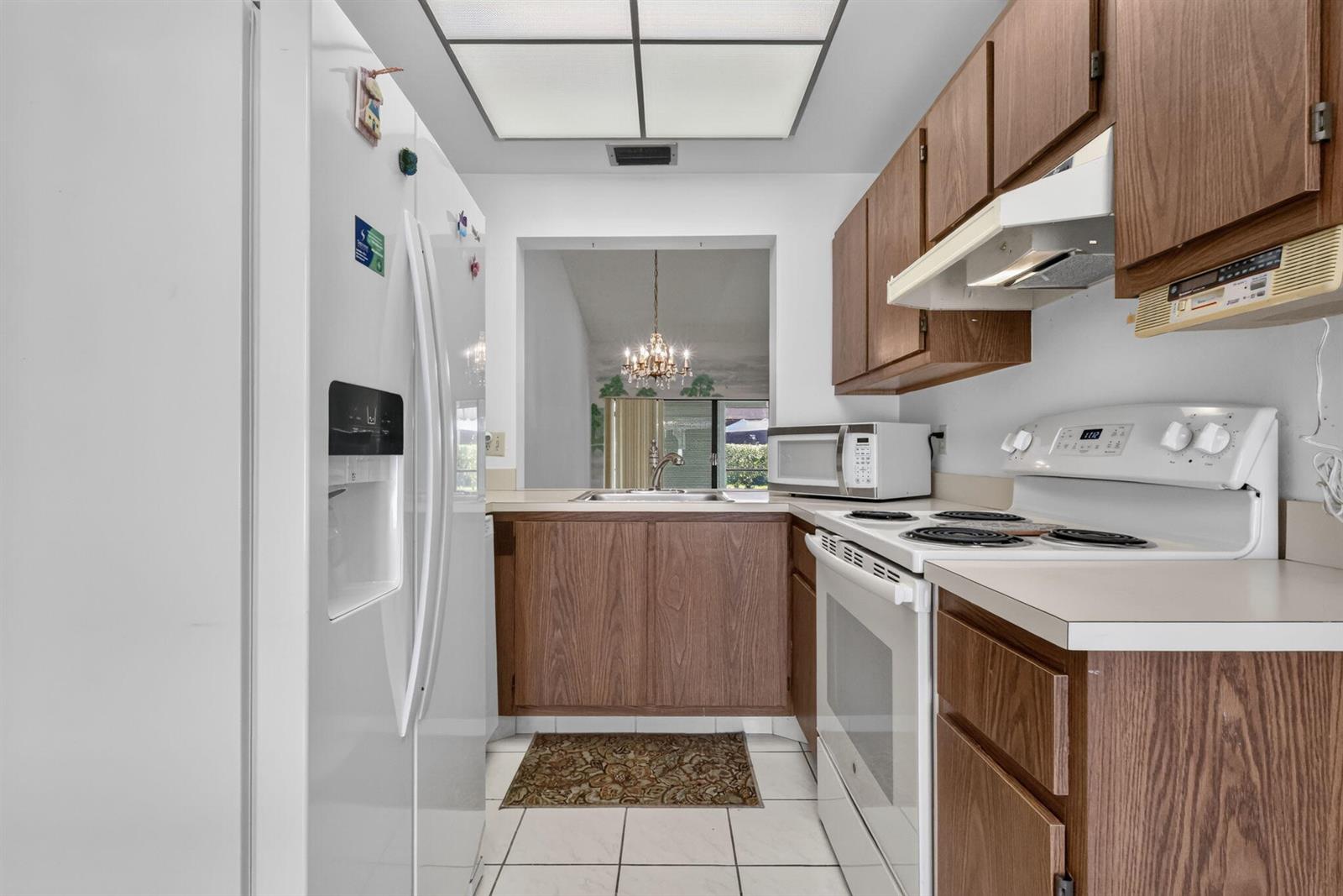 A galley kitchen features wood cabinets, white appliances, tile flooring, and a pass-through window — 3924 San Anselmo Drive # B, Lake Worth FL 33467, LAKE WORTH, FL