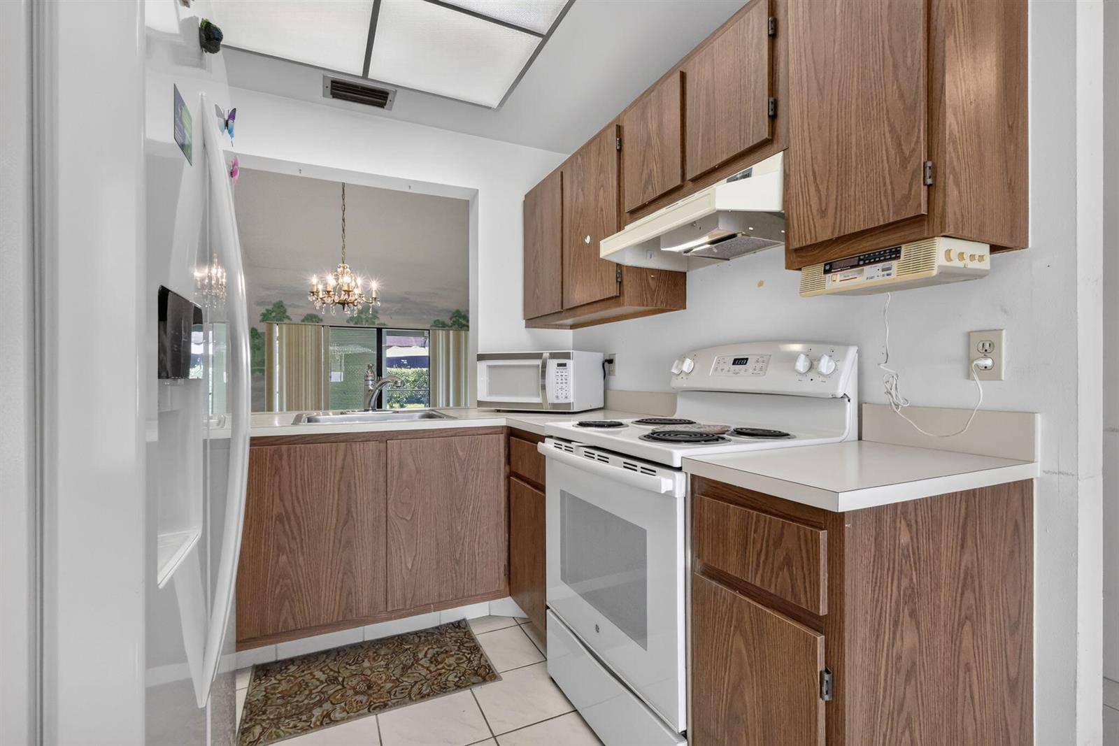 A kitchen features wood cabinets, white appliances, a tiled floor, and a pass-through window — 3924 San Anselmo Drive # B, Lake Worth FL 33467, LAKE WORTH, FL