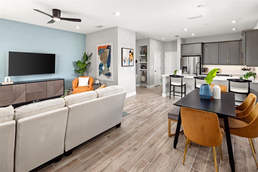 An open-concept living and dining area features a light blue accent wall, gray cabinetry, and wood-look flooring — 5100 GREENSHADE GROVE AVENUE, APOPKA, FL