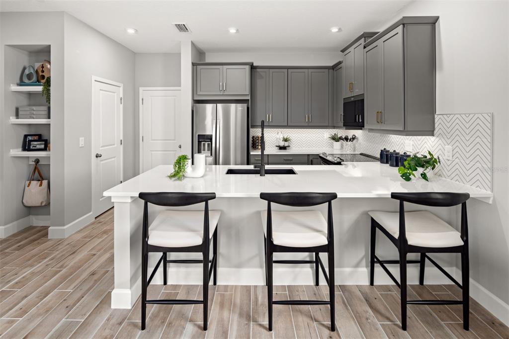 A modern kitchen features gray cabinets, a white island with bar stools, and herringbone backsplash — 5100 GREENSHADE GROVE AVENUE, APOPKA, FL