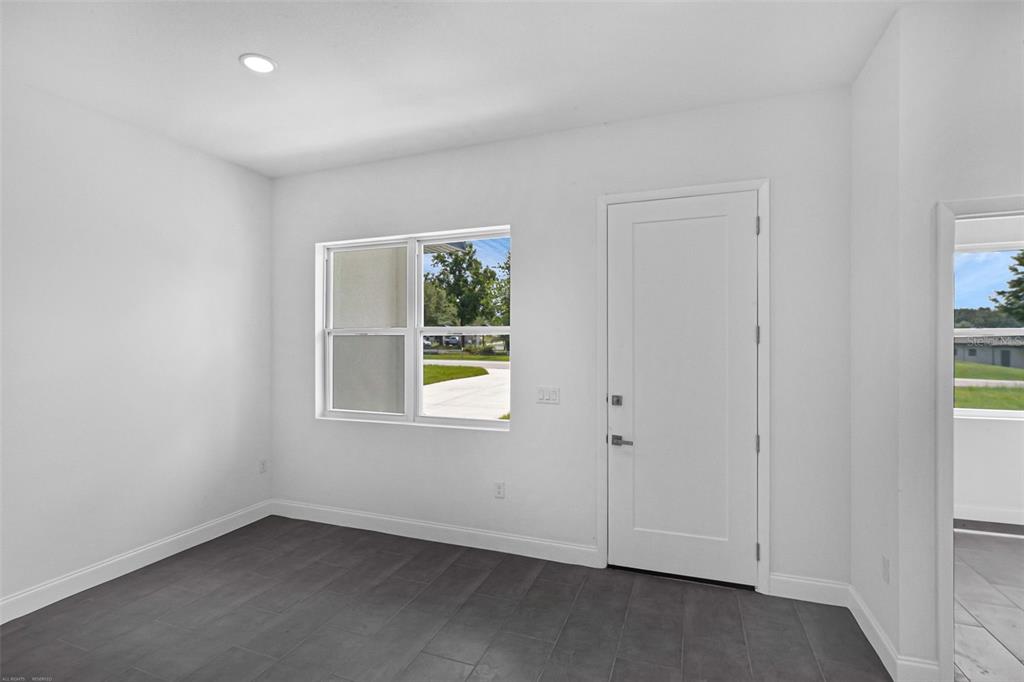 A room with white walls, dark tile flooring, a window, and a white door — 20563 SW RAINBOW LAKES BOULEVARD, DUNNELLON, FL