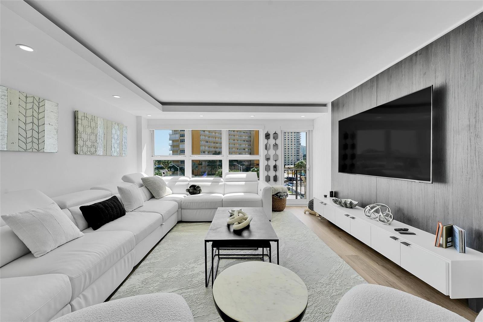 A modern living room features a white sectional sofa, a large television, and floor-to-ceiling windows — 405 N Ocean Boulevard # 306, Pompano Beach FL 33062, POMPANO BEACH, FL