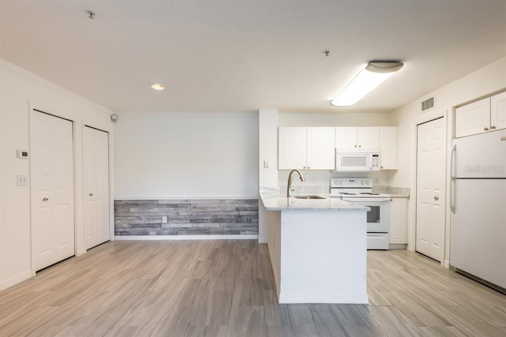 A kitchen with white cabinets, a breakfast bar, and wood-look flooring next to a dining area — 4209 WOODSTORKS WALK WAY UNIT 1110, LUTZ, FL