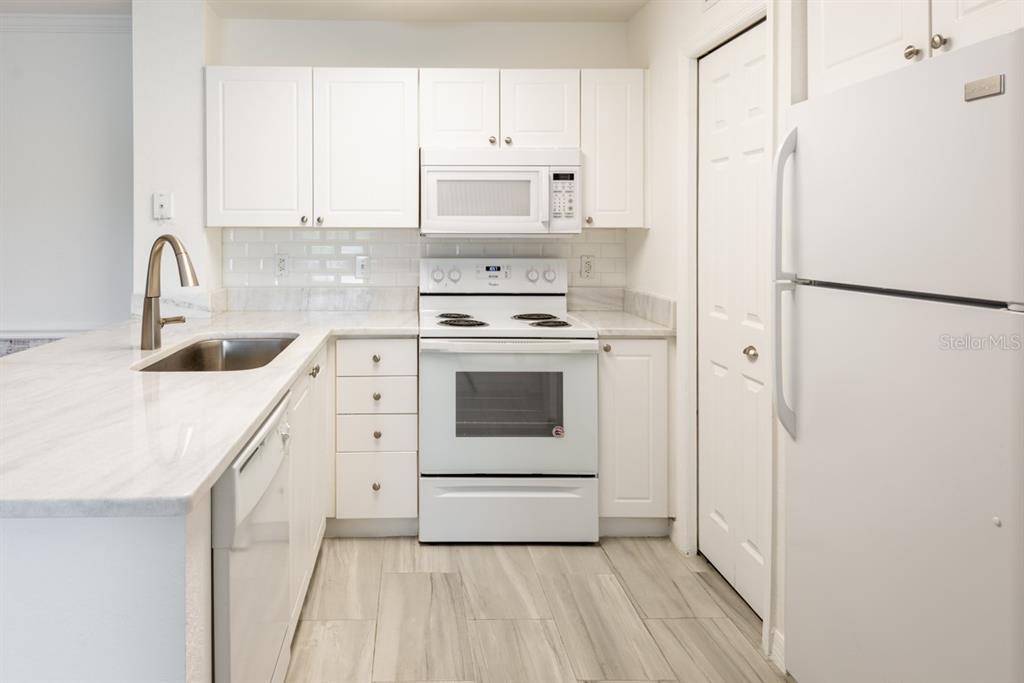 A white kitchen features a stainless steel sink, white appliances, and light-colored stone countertops — 4209 WOODSTORKS WALK WAY UNIT 1110, LUTZ, FL