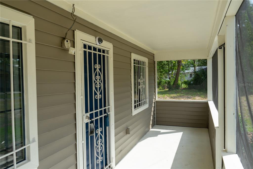 A covered porch with gray siding, a white security door, and window bars — 1307 RAILROAD AVENUE, SANFORD, FL