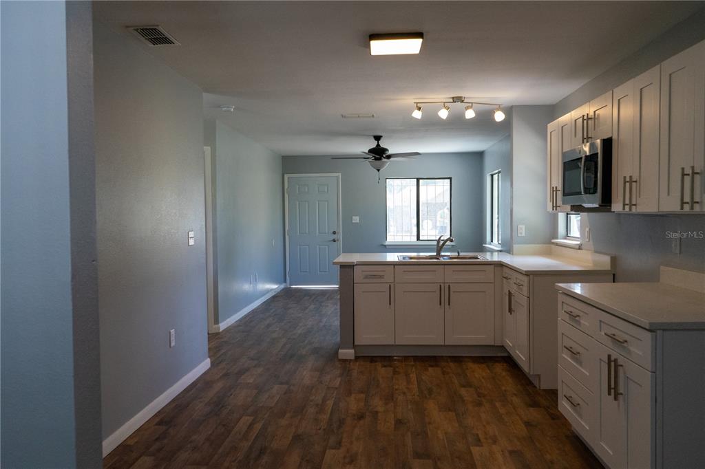 A kitchen with white cabinets, light countertops, and wood-look flooring opens to an entryway — 1307 RAILROAD AVENUE, SANFORD, FL