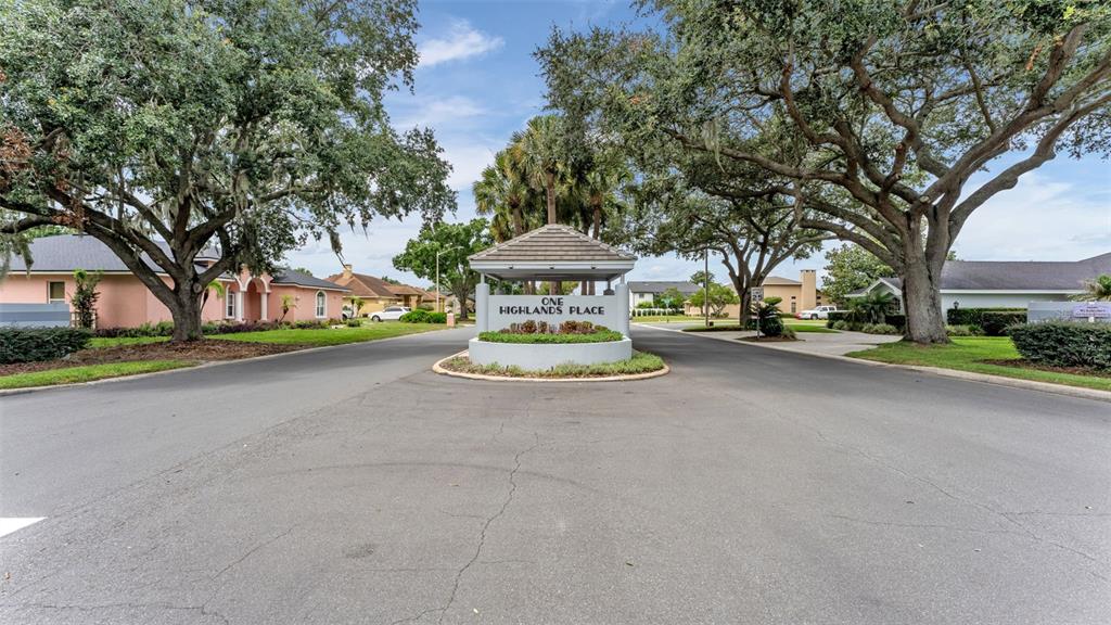 A paved road leads to a gated community entrance sign labeled One Highlands Place — 4765 HIGHLANDS PLACE CIRCLE, LAKELAND, FL