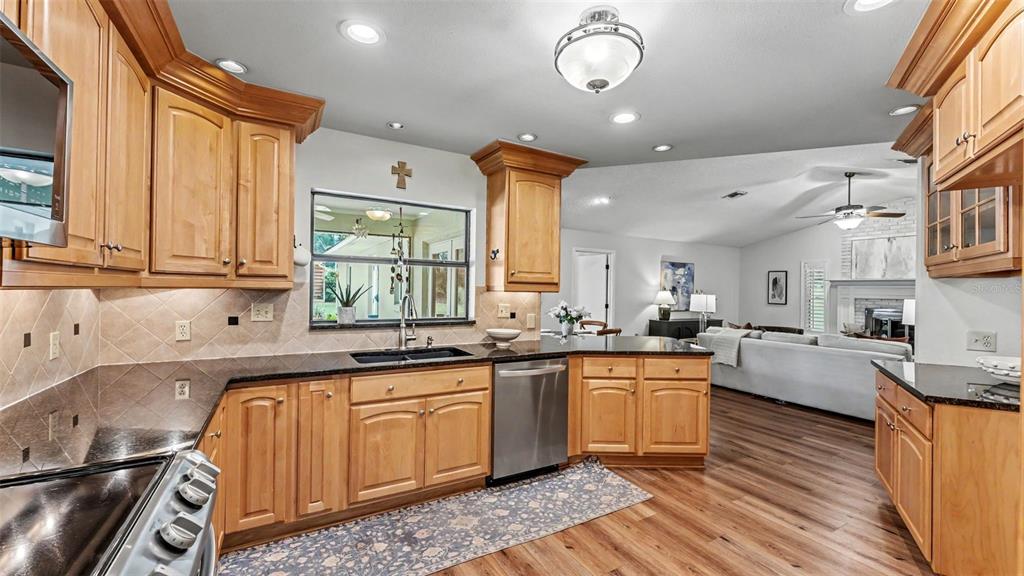 A kitchen with light wood cabinets, black countertops, stainless steel appliances, and an open floor plan — 4765 HIGHLANDS PLACE CIRCLE, LAKELAND, FL