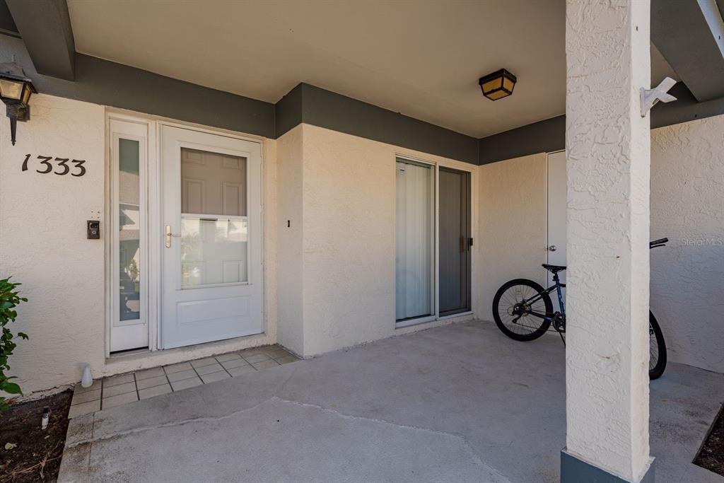 A covered concrete entryway features a front door, a sliding glass door, and a bicycle — 1333 N MCMULLEN BOOTH ROAD UNIT 1333, CLEARWATER, FL