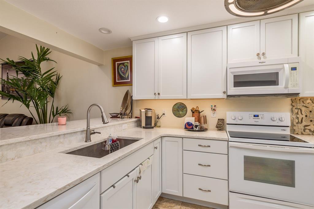 A kitchen features white cabinets, light countertops, a stainless steel sink, and white appliances — 1333 N MCMULLEN BOOTH ROAD UNIT 1333, CLEARWATER, FL