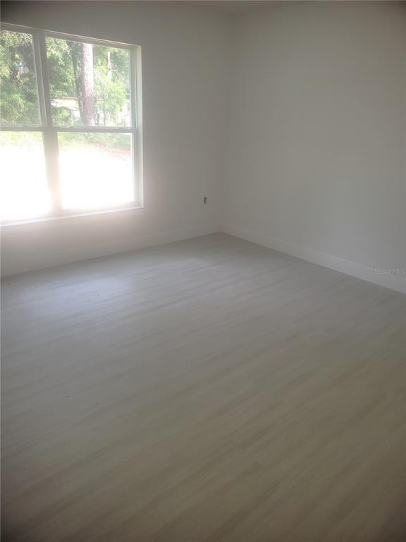 A hallway with light-colored flooring leads toward a bright doorway in the distance — 338 2ND WAY, INTERLACHEN, FL