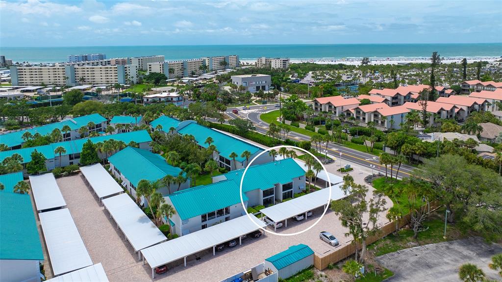 An aerial view shows a multi-story residential building with a teal roof and covered parking — 5641 MIDNIGHT PASS ROAD UNIT 902, SARASOTA, FL