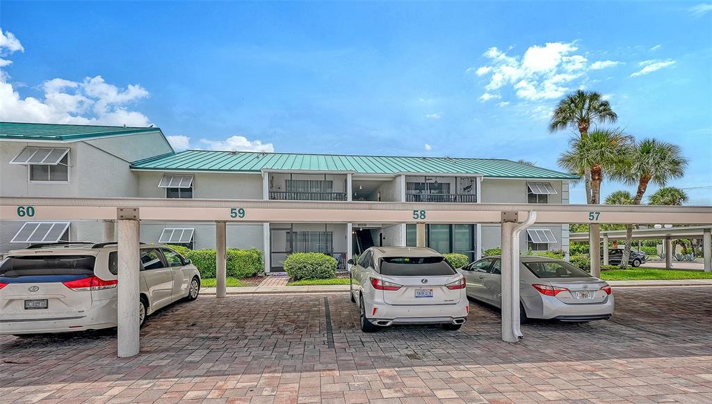 A covered parking area sits in front of a two-story apartment building with green roofs — 5641 MIDNIGHT PASS ROAD UNIT 902, SARASOTA, FL