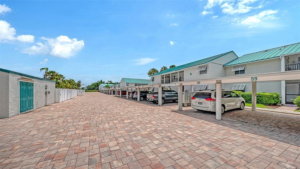 A paved parking area with covered carports sits in front of multi-story residential buildings — 5641 MIDNIGHT PASS ROAD UNIT 902, SARASOTA, FL