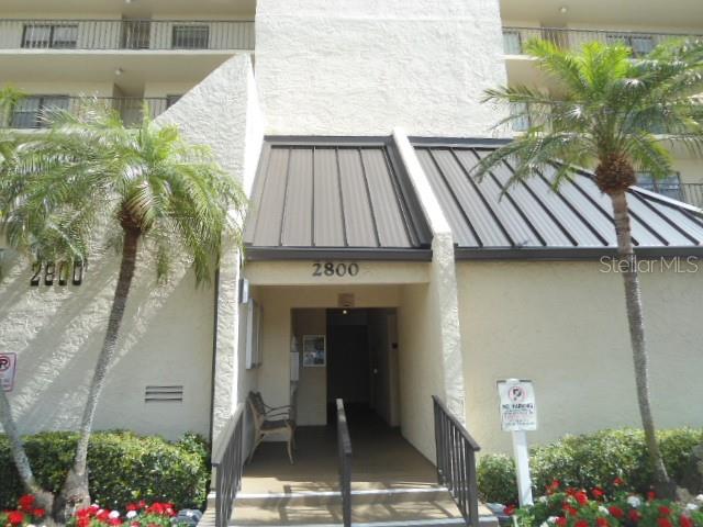 Exterior view of a multi-story building entrance with a metal roof and palm trees — 2800 COVE CAY DRIVE UNIT 4D, CLEARWATER, FL