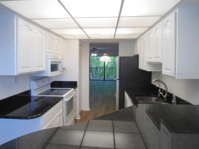 A kitchen with white cabinets, black countertops, and a view into a living area — 2800 COVE CAY DRIVE UNIT 4D, CLEARWATER, FL
