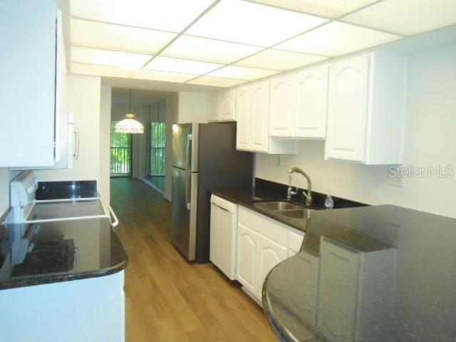 A kitchen with white cabinets, dark countertops, stainless steel appliances, and wood-look flooring — 2800 COVE CAY DRIVE UNIT 4D, CLEARWATER, FL
