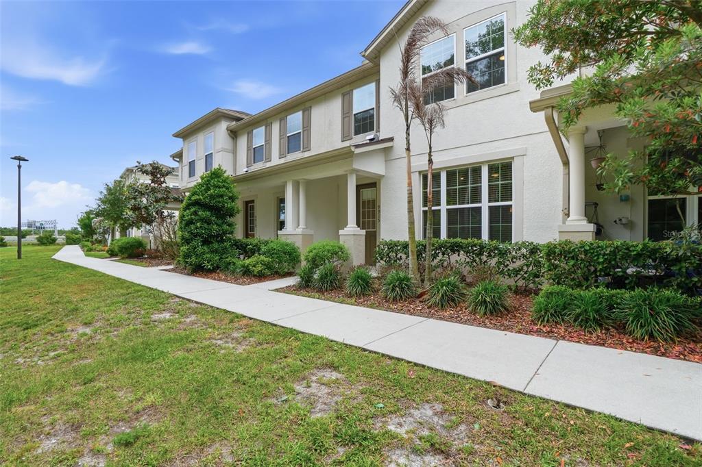 A two-story townhouse exterior with a covered front porch, tan stucco siding, and landscaped yard — 9915 HIGHLAND SKY ALLEY, ORLANDO, FL