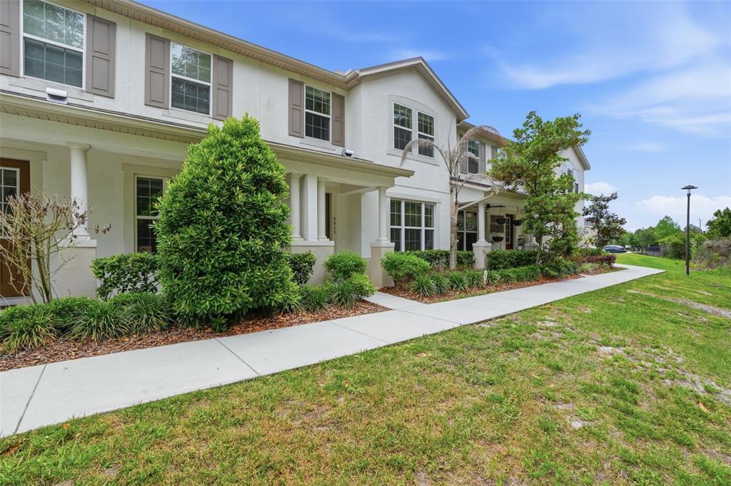 A two-story townhouse exterior with white stucco walls, dark shutters, and a concrete walkway — 9915 HIGHLAND SKY ALLEY, ORLANDO, FL