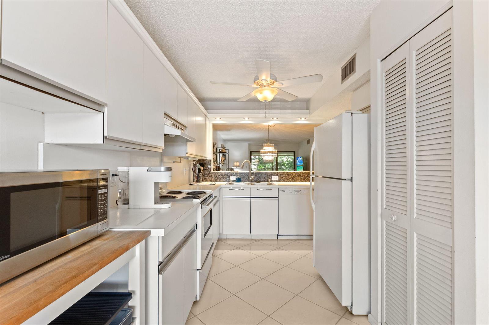 A galley-style kitchen features white cabinetry, a white refrigerator, and light-colored tile flooring — 5380 Cedar Lake Drive # 303, Boynton Beach FL 33437, BOYNTON BEACH, FL