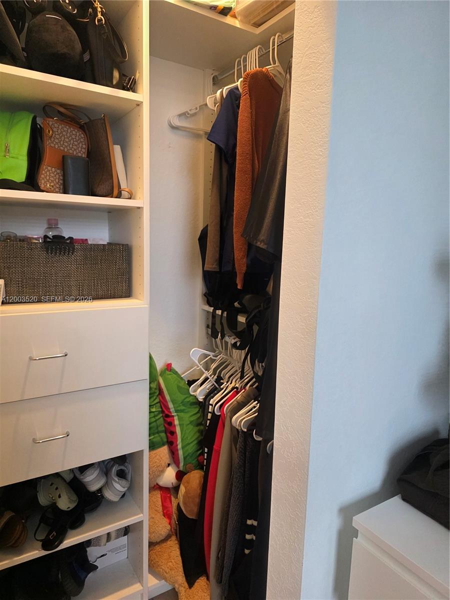A closet features built-in white shelving, drawers, and a hanging rod with clothes — 23231 SW 129th Path # 0, Homestead FL 33170, HOMESTEAD, FL