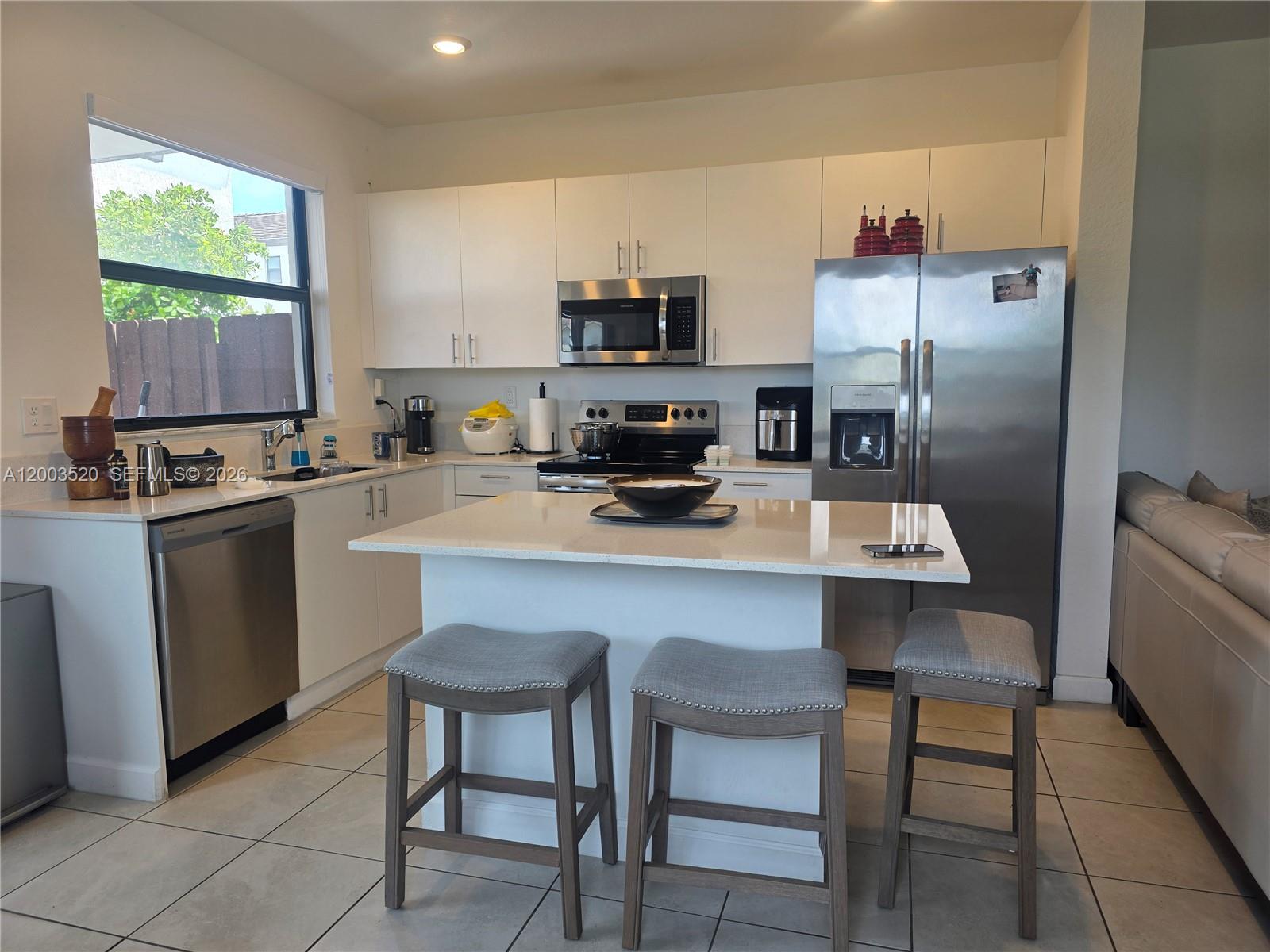 A kitchen features white cabinets, stainless steel appliances, a central island, and three bar stools — 23231 SW 129th Path # 0, Homestead FL 33170, HOMESTEAD, FL