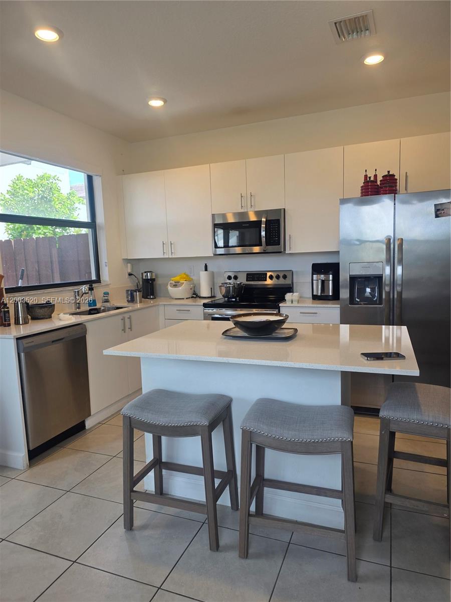A kitchen features white cabinets, stainless steel appliances, a quartz island, and tile flooring — 23231 SW 129th Path # 0, Homestead FL 33170, HOMESTEAD, FL