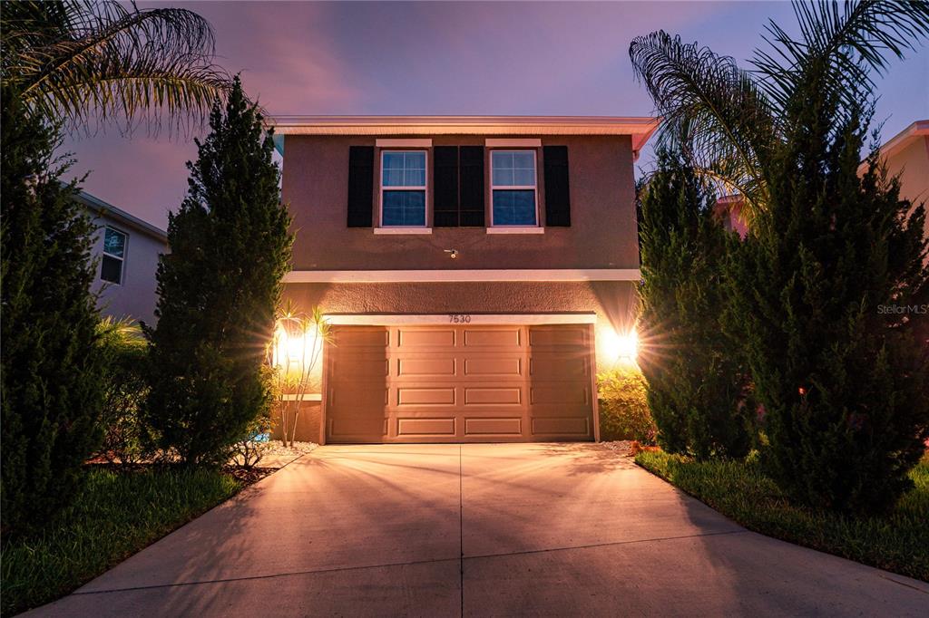 A two-story house exterior features a two-car garage, driveway, and palm trees at dusk — 7530 CYPRESS WALK DRIVE, NEW PORT RICHEY, FL