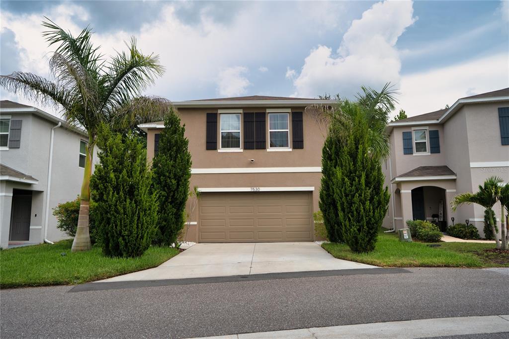 A two-story tan house with a two-car garage and two tall evergreen trees — 7530 CYPRESS WALK DRIVE, NEW PORT RICHEY, FL
