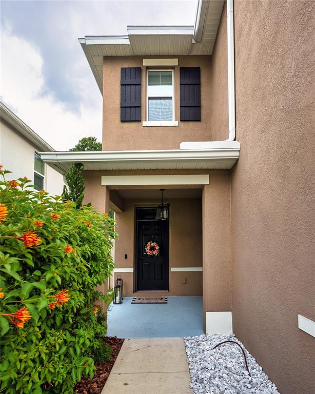The exterior of a two-story tan stucco home features a covered entryway and black shutters — 7530 CYPRESS WALK DRIVE, NEW PORT RICHEY, FL