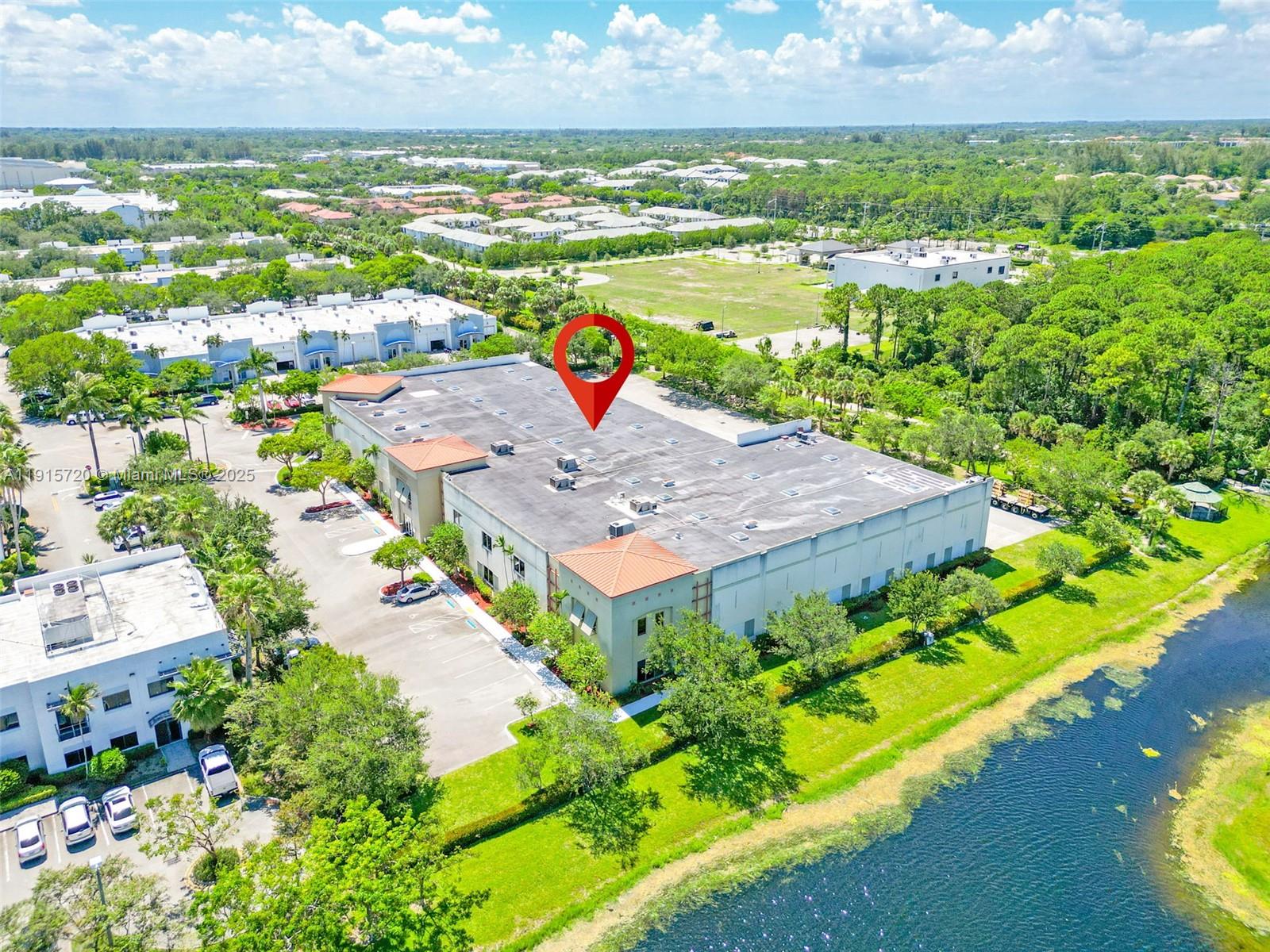 An aerial view shows a commercial building with a red-tiled roof beside a lake — 6850 Lyons Technology Cir, Coconut Creek FL 33073, COCONUT CREEK, FL