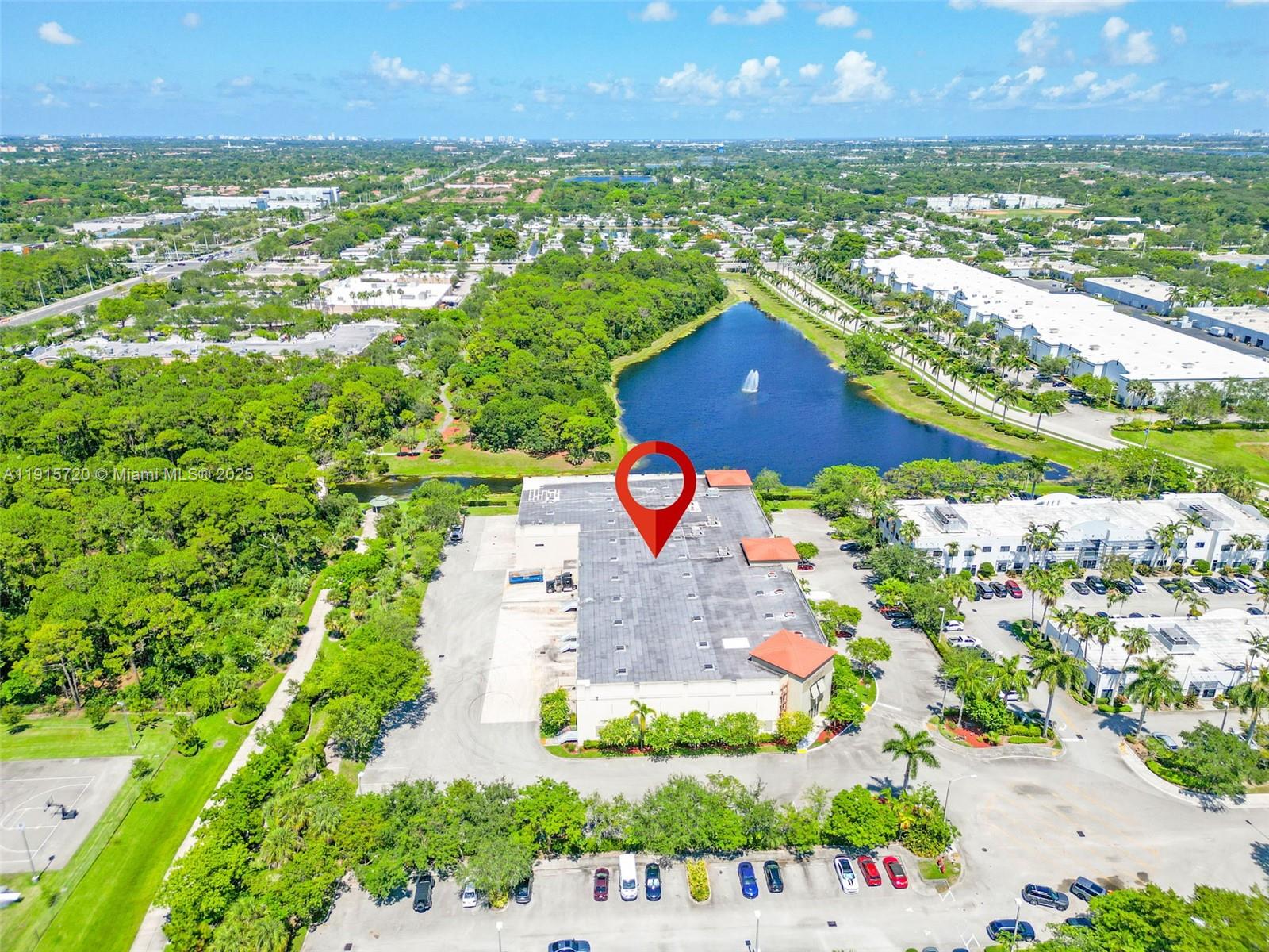An aerial view shows a commercial building with a flat roof next to a lake — 6850 Lyons Technology Cir, Coconut Creek FL 33073, COCONUT CREEK, FL