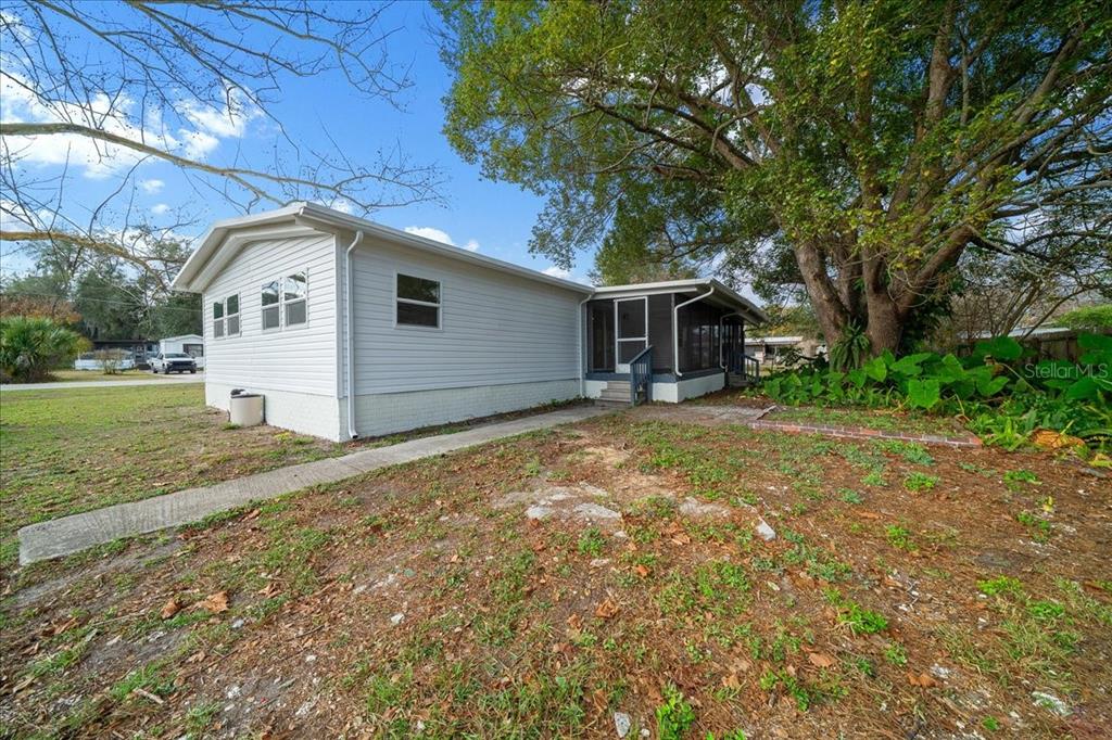 A white mobile home with a screened-in porch sits on a grassy lot with trees — 13219 32ND COURT, BELLEVIEW, FL