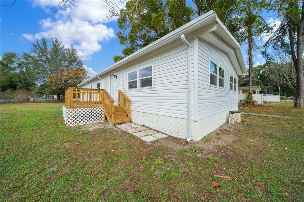 A white single-story house with a wooden deck and stairs sits on a grassy lot — 13219 32ND COURT, BELLEVIEW, FL