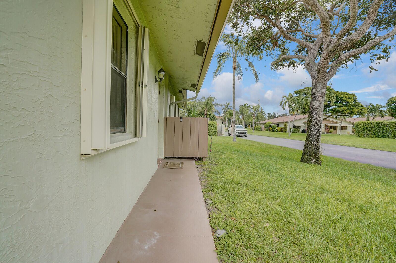 A side view of a light green house with a concrete walkway and privacy screen — 1737 Palmland Drive, Boynton Beach FL 33436, BOYNTON BEACH, FL
