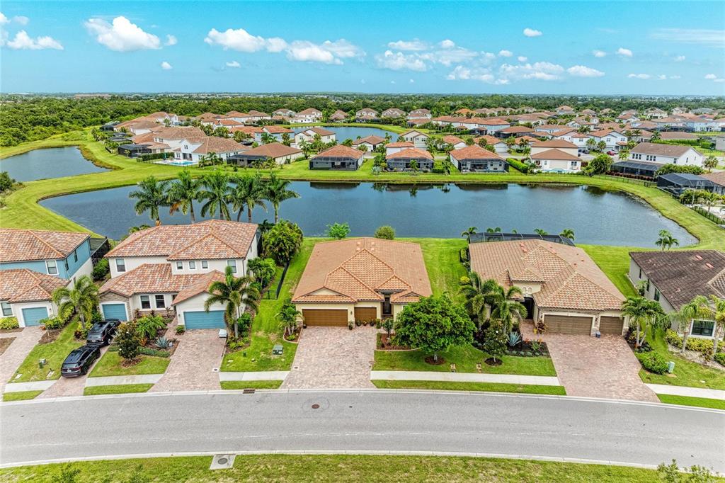 An aerial view shows three suburban houses with tile roofs situated along a lake — 3512 SAVANNA PALMS COURT, BRADENTON, FL