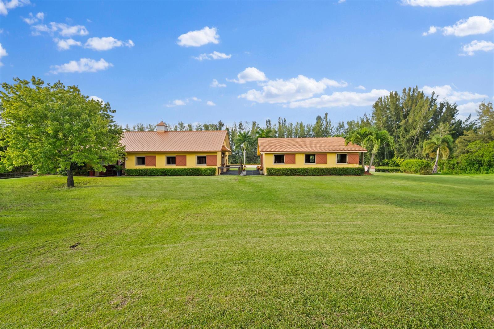 Two yellow buildings with brown roofs sit on a large, grassy lawn under a sky — 11861 Hawk Hollow, Wellington FL 33449, WELLINGTON, FL