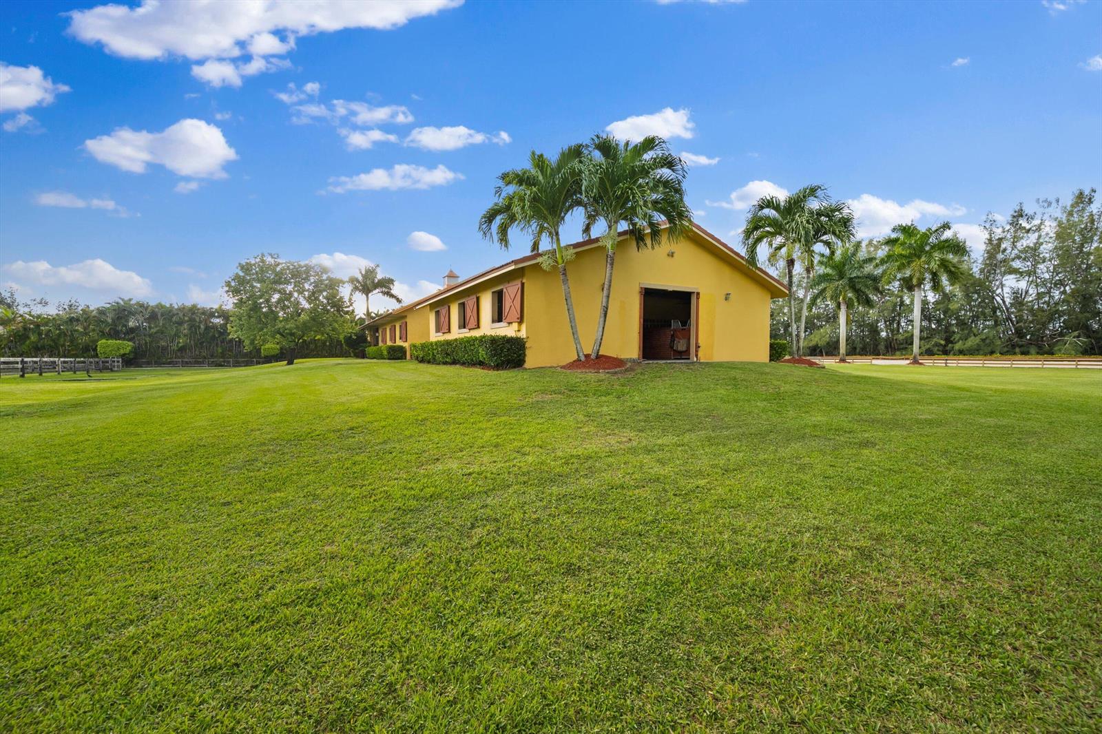 A yellow barn sits on a large, grassy lawn under a blue sky with clouds — 11861 Hawk Hollow, Wellington FL 33449, WELLINGTON, FL